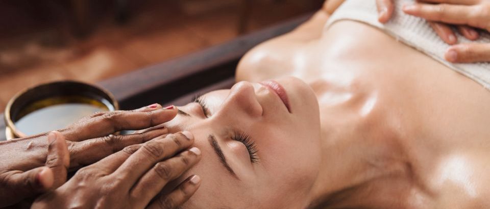 Ayurvedic face massage with oil on the wooden table